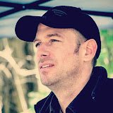 Adam Wallington wearing a dark baseball cap, looking off to the side.